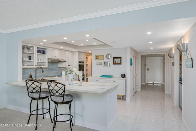 kitchen featuring a peninsula, a breakfast bar area, white cabinets, and decorative backsplash