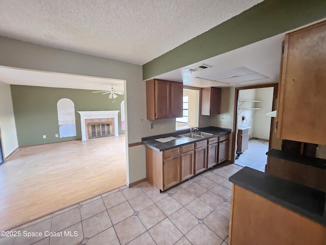 kitchen with sink, light tile patterned floors, ceiling fan, a textured ceiling, and a tiled fireplace