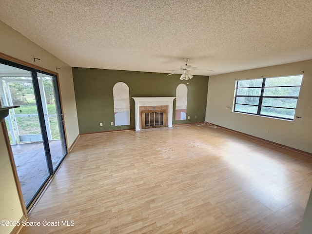 unfurnished living room featuring ceiling fan, a tile fireplace, a healthy amount of sunlight, and light wood-type flooring