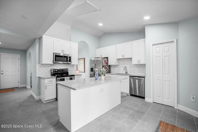 kitchen with lofted ceiling, sink, appliances with stainless steel finishes, a kitchen island, and white cabinets