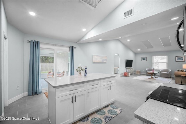 kitchen with a kitchen island, lofted ceiling, white cabinets, light stone countertops, and electric stove