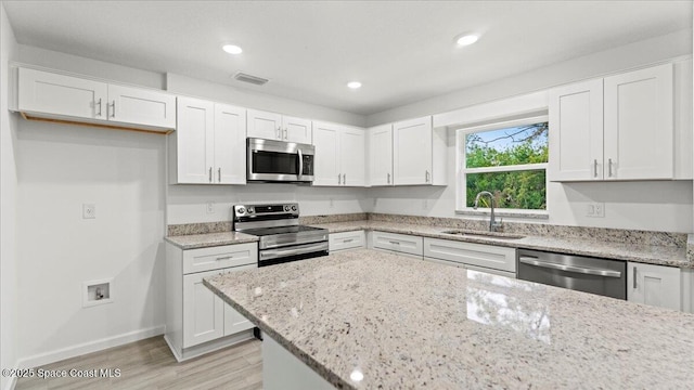 kitchen with light stone counters, stainless steel appliances, sink, and white cabinets