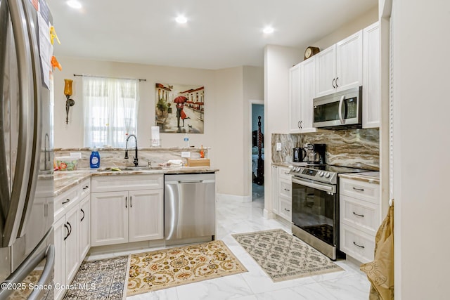 kitchen with sink, white cabinets, backsplash, stainless steel appliances, and light stone countertops