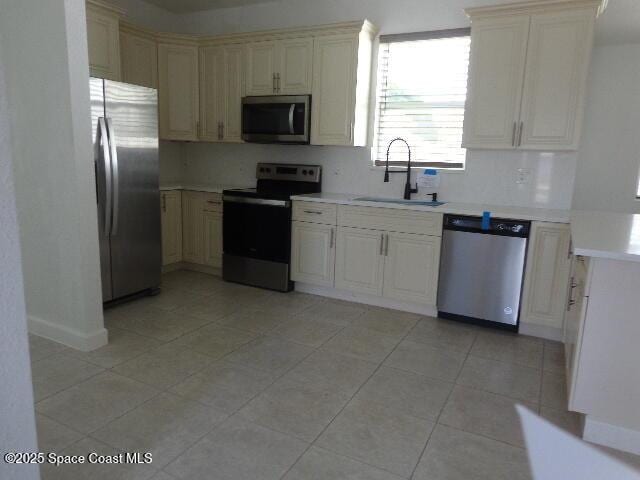 kitchen with cream cabinets, appliances with stainless steel finishes, sink, and light tile patterned floors