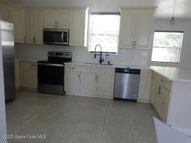 kitchen featuring pendant lighting, sink, light tile patterned floors, stainless steel appliances, and cream cabinets