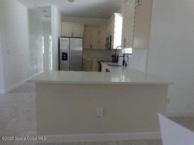 kitchen with sink, light tile patterned floors, appliances with stainless steel finishes, cream cabinets, and kitchen peninsula