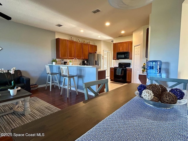 kitchen featuring a kitchen bar, sink, wood-type flooring, kitchen peninsula, and black appliances