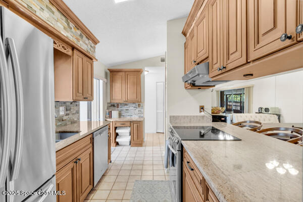 kitchen featuring lofted ceiling, stainless steel appliances, a healthy amount of sunlight, and light tile patterned flooring