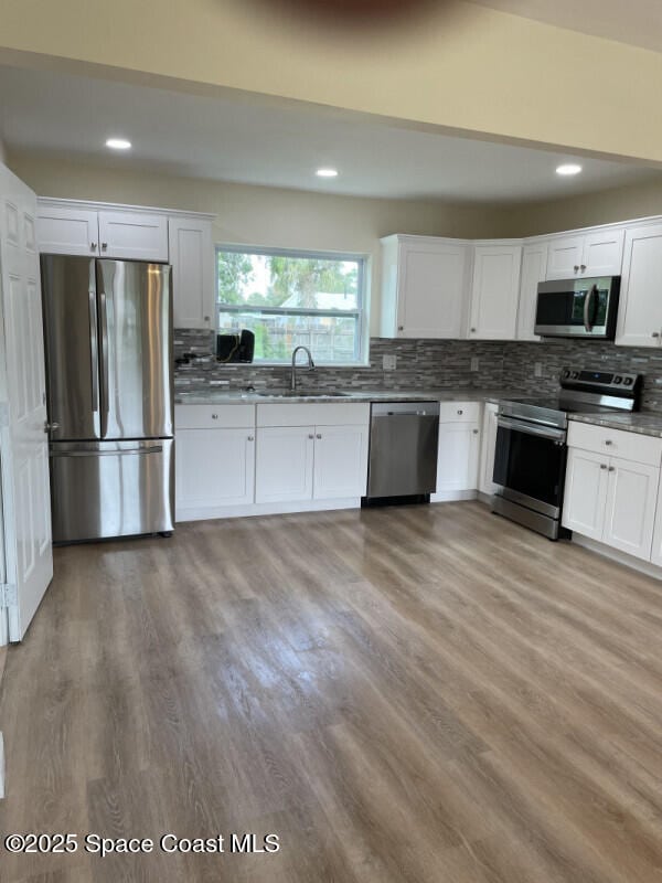 kitchen featuring white cabinetry, appliances with stainless steel finishes, light hardwood / wood-style floors, and backsplash