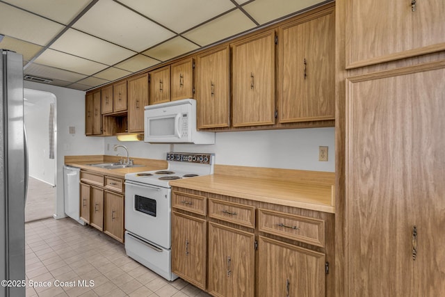 kitchen with a drop ceiling, sink, white appliances, and light tile patterned floors