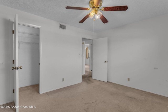 unfurnished bedroom with a walk in closet, light colored carpet, a textured ceiling, a closet, and ceiling fan