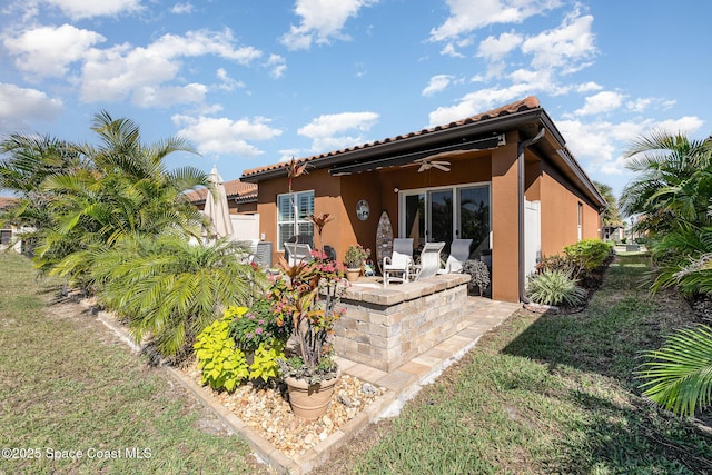 rear view of house featuring ceiling fan, a patio area, and a lawn