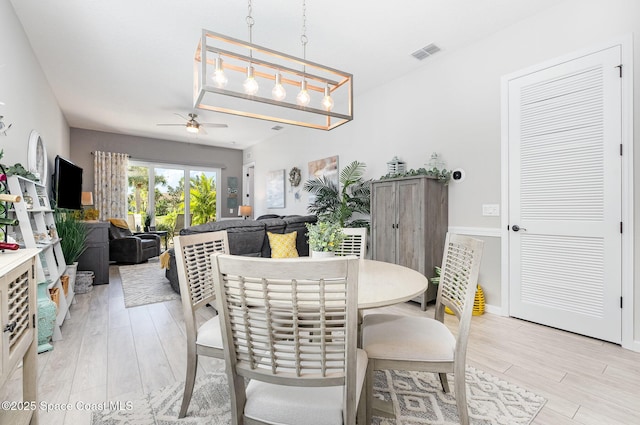 dining space with ceiling fan with notable chandelier and light hardwood / wood-style floors