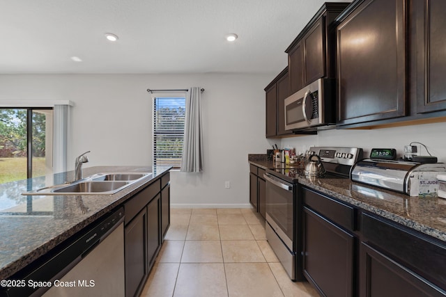 kitchen featuring appliances with stainless steel finishes, sink, dark stone counters, light tile patterned floors, and dark brown cabinetry