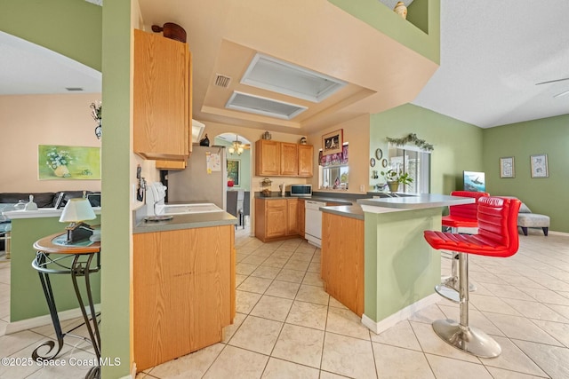 kitchen featuring a kitchen bar, light tile patterned floors, stainless steel fridge, kitchen peninsula, and a raised ceiling