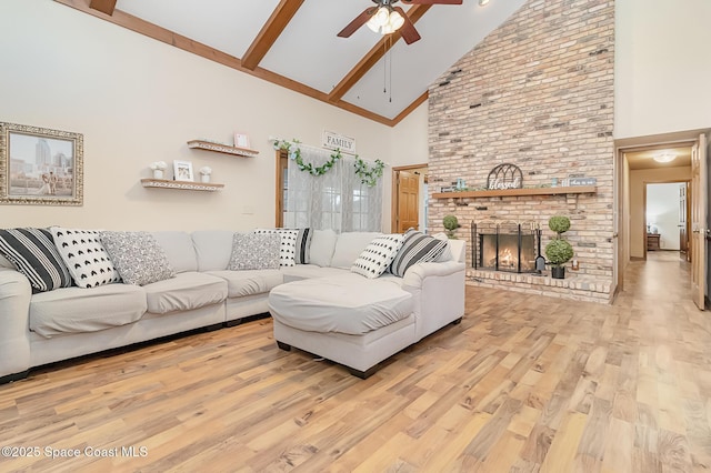 living room featuring ceiling fan, high vaulted ceiling, light hardwood / wood-style floors, a brick fireplace, and beamed ceiling