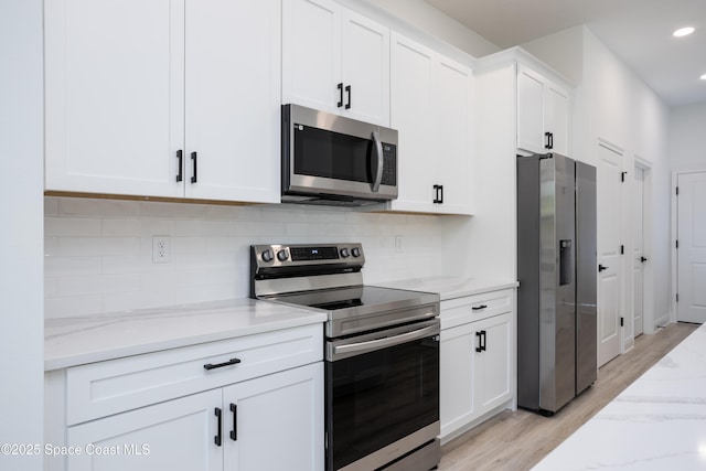 kitchen with light hardwood / wood-style flooring, appliances with stainless steel finishes, light stone counters, white cabinets, and decorative backsplash