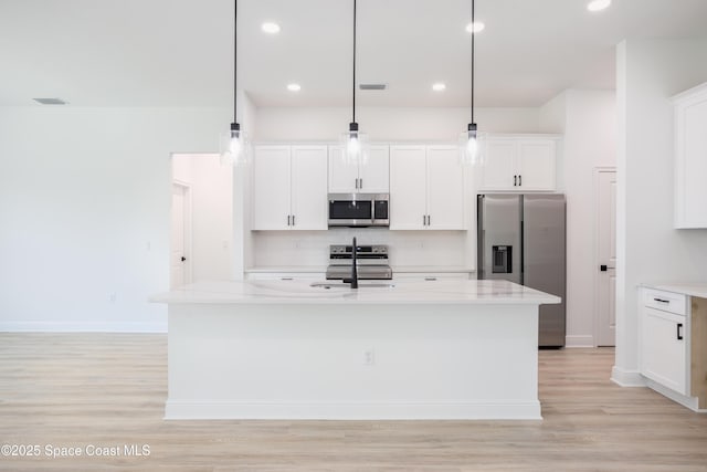 kitchen with a kitchen island with sink, hanging light fixtures, white cabinetry, stainless steel appliances, and light stone countertops