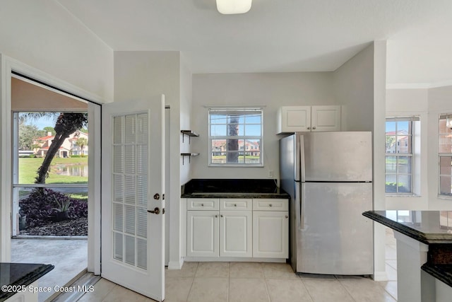 kitchen featuring dark stone countertops, light tile patterned floors, white cabinets, and stainless steel refrigerator