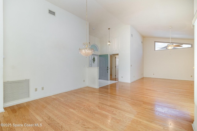 empty room featuring high vaulted ceiling, ceiling fan with notable chandelier, and light wood-type flooring