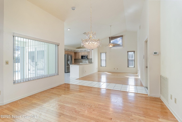 unfurnished living room with high vaulted ceiling, ceiling fan with notable chandelier, and light wood-type flooring