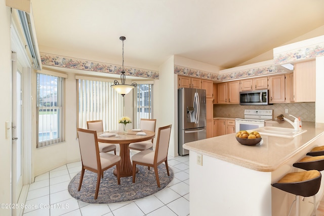 kitchen featuring light brown cabinetry, vaulted ceiling, hanging light fixtures, kitchen peninsula, and stainless steel appliances