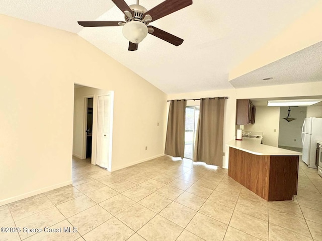 kitchen with light tile patterned floors, a peninsula, vaulted ceiling, light countertops, and freestanding refrigerator