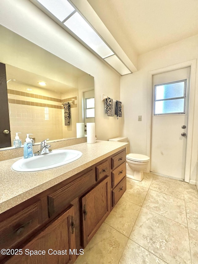 bathroom featuring tile patterned flooring, vanity, a tile shower, and toilet