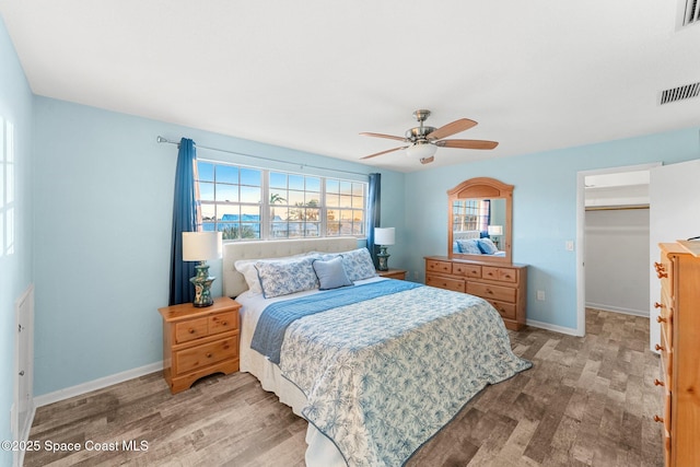 bedroom with a spacious closet, a closet, ceiling fan, and light wood-type flooring