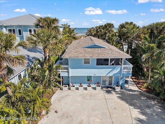 raised beach house featuring a balcony, a water view, and french doors