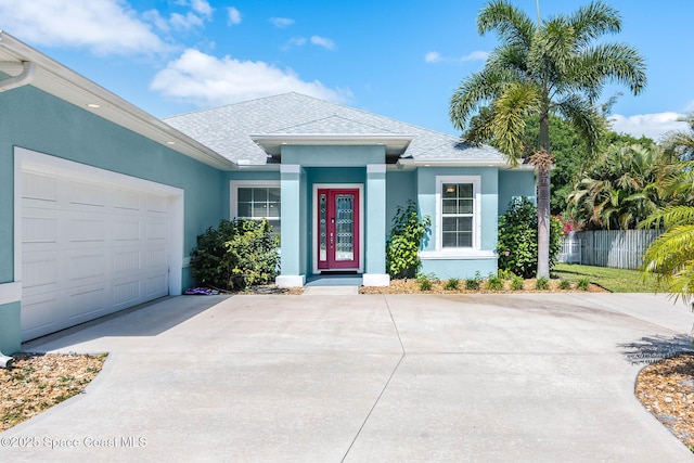 ranch-style home featuring concrete driveway, a shingled roof, stucco siding, fence, and an attached garage