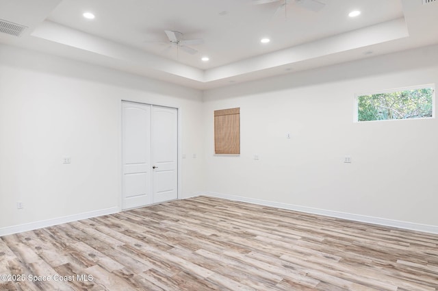 spare room featuring a ceiling fan, a tray ceiling, light wood-style floors, baseboards, and recessed lighting