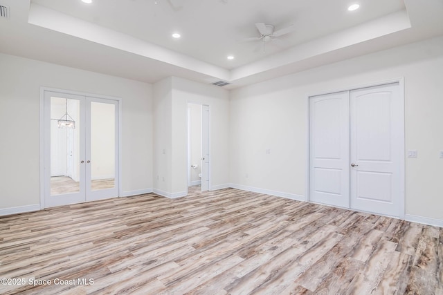 unfurnished bedroom with a raised ceiling, light wood-type flooring, recessed lighting, baseboards, and french doors