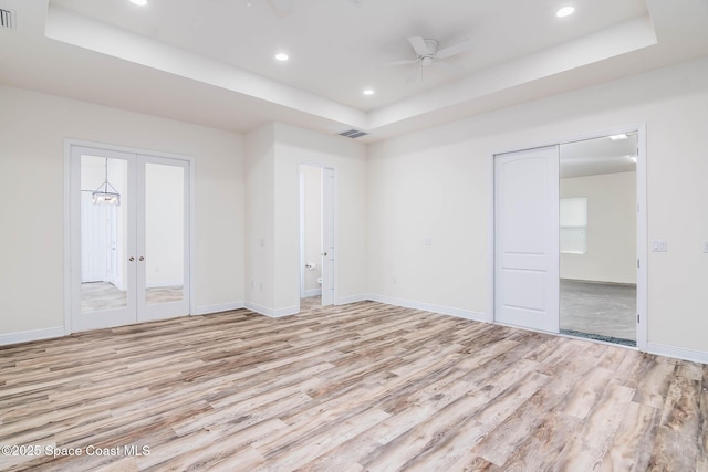 unfurnished bedroom with a tray ceiling, light wood-style floors, recessed lighting, baseboards, and french doors