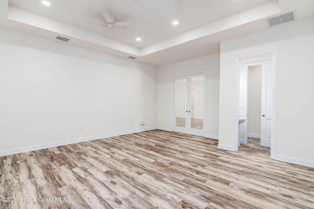unfurnished bedroom with a raised ceiling, french doors, light wood-style floors, baseboards, and recessed lighting