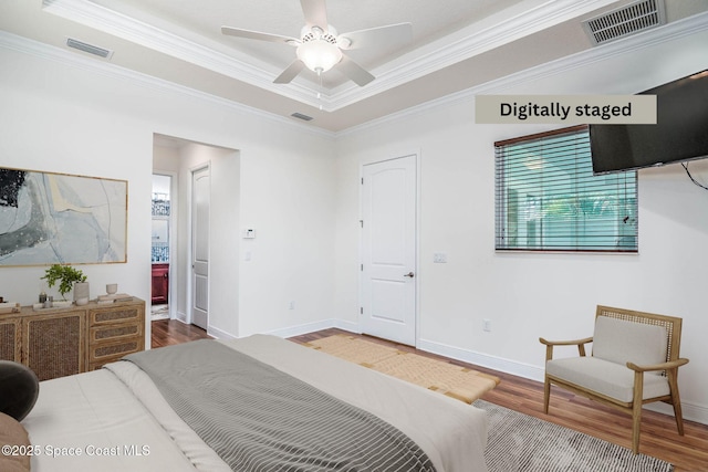 bedroom featuring wood finished floors, crown molding, a tray ceiling, baseboards, and connected bathroom