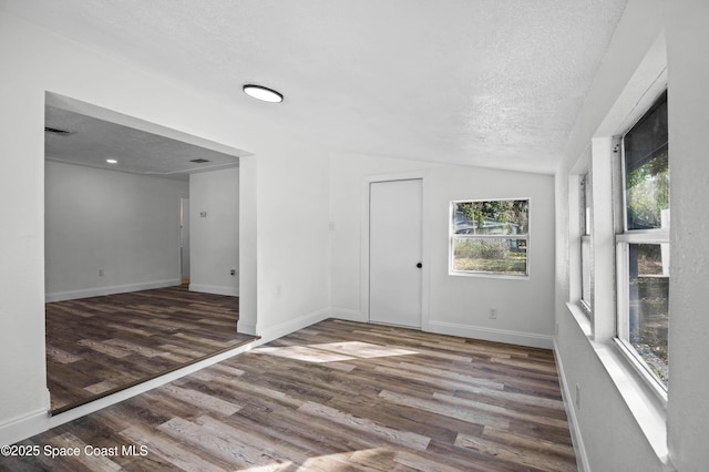 empty room with dark hardwood / wood-style flooring, vaulted ceiling, and a textured ceiling