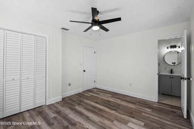 unfurnished bedroom with ceiling fan, dark hardwood / wood-style floors, connected bathroom, a textured ceiling, and a closet