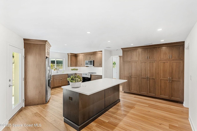 kitchen with sink, a breakfast bar area, appliances with stainless steel finishes, a kitchen island, and light wood-type flooring