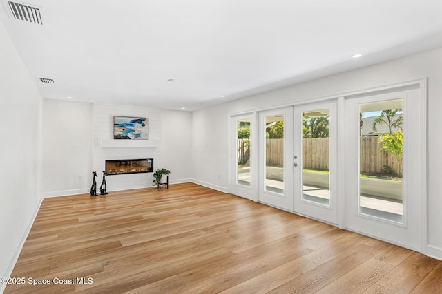 unfurnished living room with a large fireplace, light hardwood / wood-style floors, and french doors