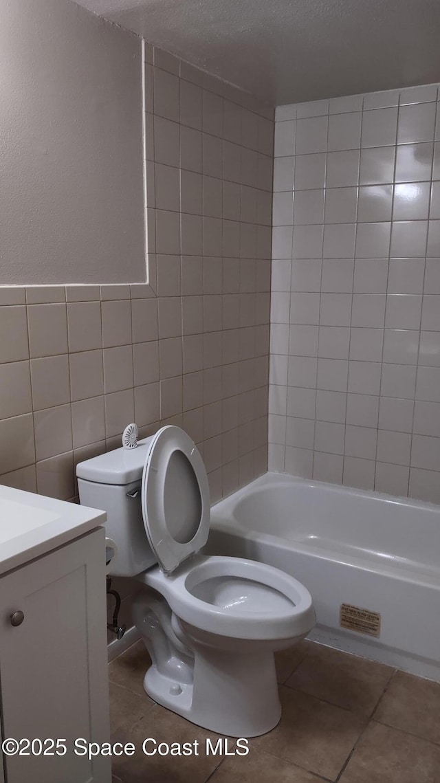 full bathroom with tile walls, tile patterned flooring, vanity, tiled shower / bath combo, and toilet