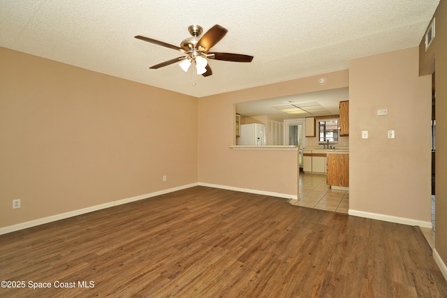 unfurnished living room with ceiling fan, a textured ceiling, light wood-style flooring, visible vents, and baseboards