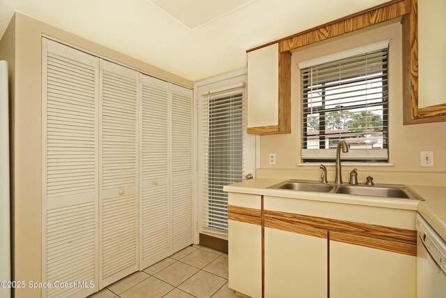 kitchen with light tile patterned flooring, a sink, white cabinetry, light countertops, and dishwasher