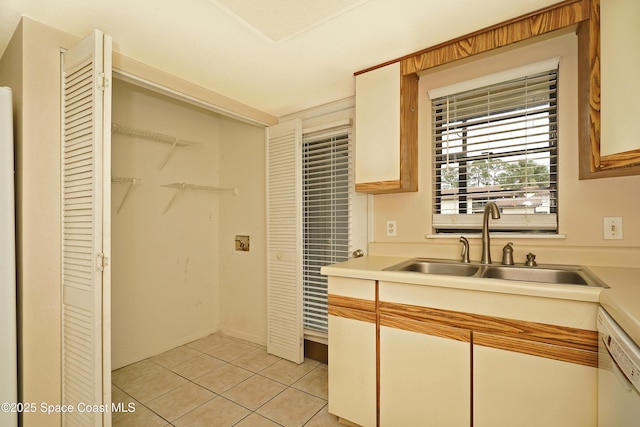 kitchen with light tile patterned floors, light countertops, white cabinets, a sink, and white dishwasher