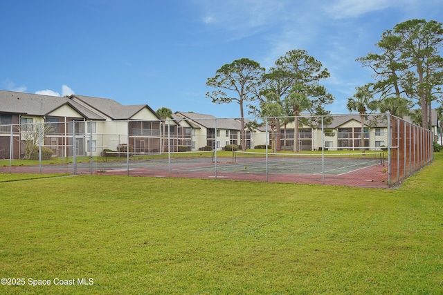 view of tennis court with a yard, a residential view, and fence