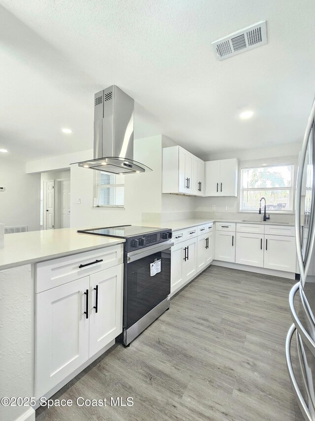 kitchen with white cabinetry, range with electric stovetop, light hardwood / wood-style floors, island exhaust hood, and kitchen peninsula