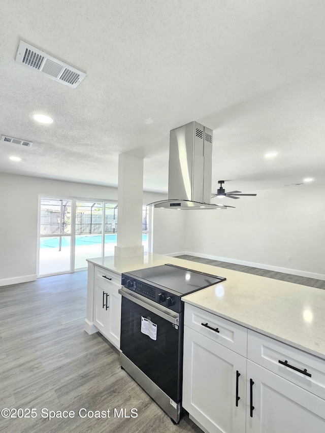 kitchen with white cabinetry, island range hood, light hardwood / wood-style floors, a textured ceiling, and stainless steel electric range oven