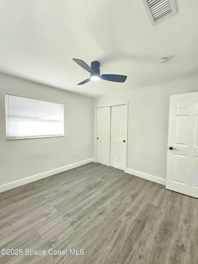 unfurnished bedroom with ceiling fan, hardwood / wood-style floors, a closet, and a textured ceiling