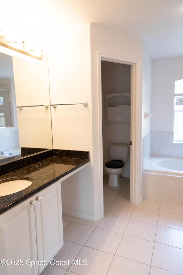 bathroom featuring tile patterned flooring, vanity, a relaxing tiled tub, and toilet