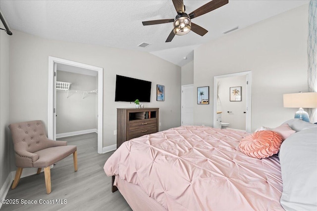 bedroom featuring a walk in closet, vaulted ceiling, a textured ceiling, light wood-type flooring, and a closet